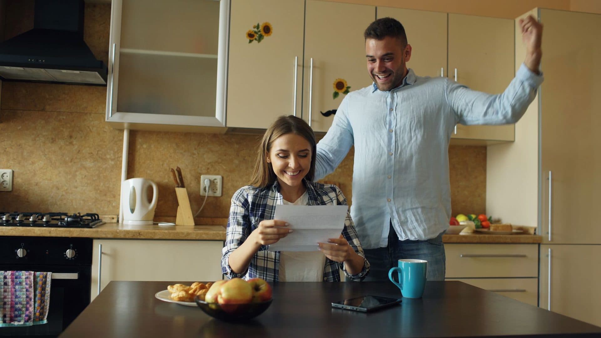 A couple in their kitchen reading a letter and celebrating