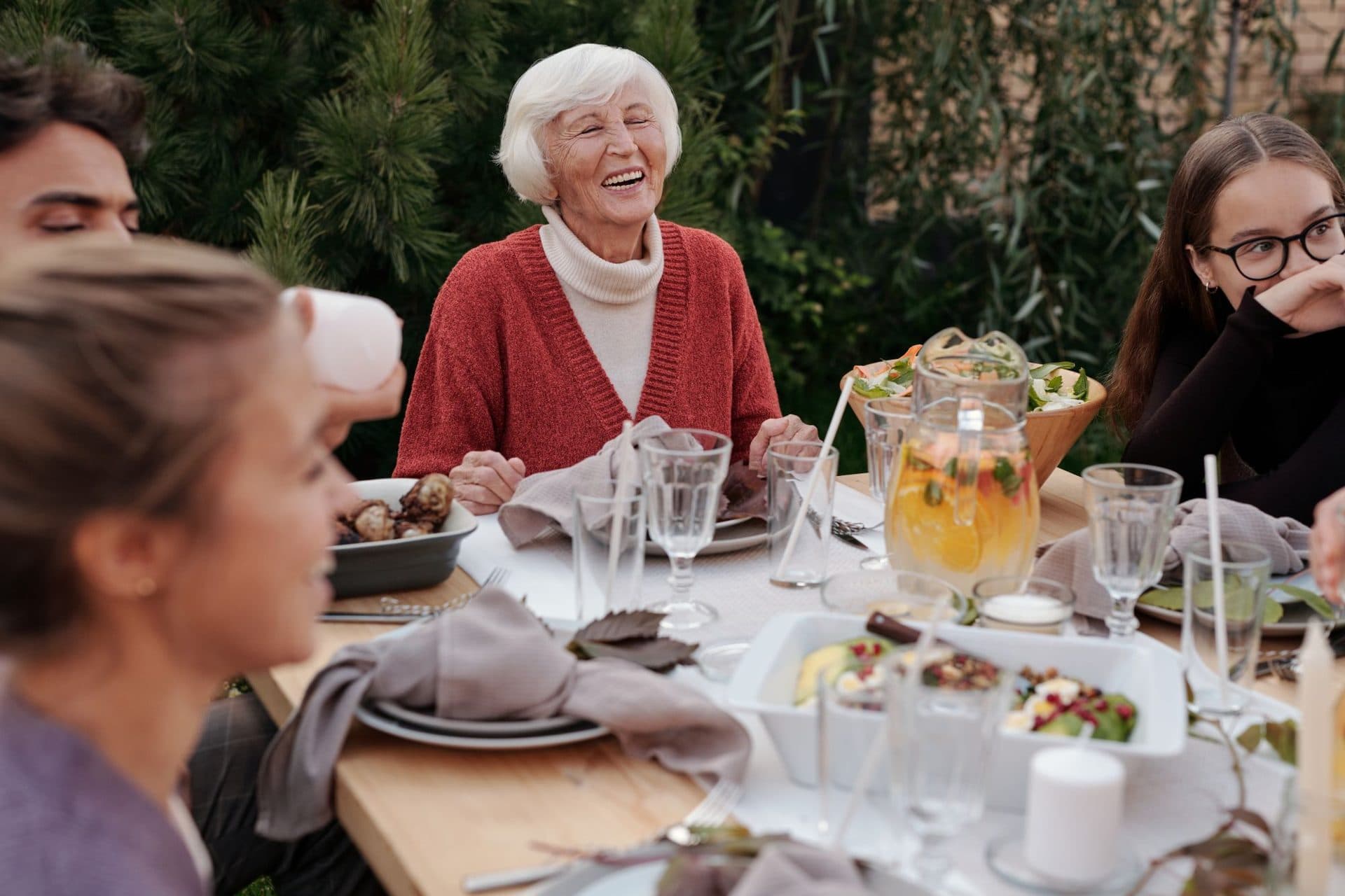 An older woman laughing with family at an outdoor dinner