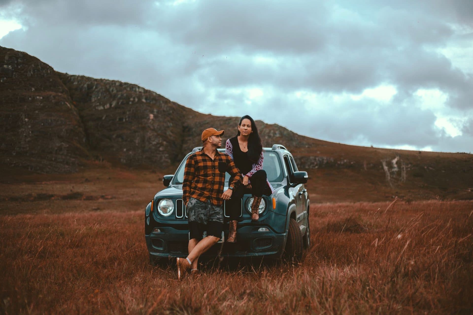 A couple sitting on their car in an open field