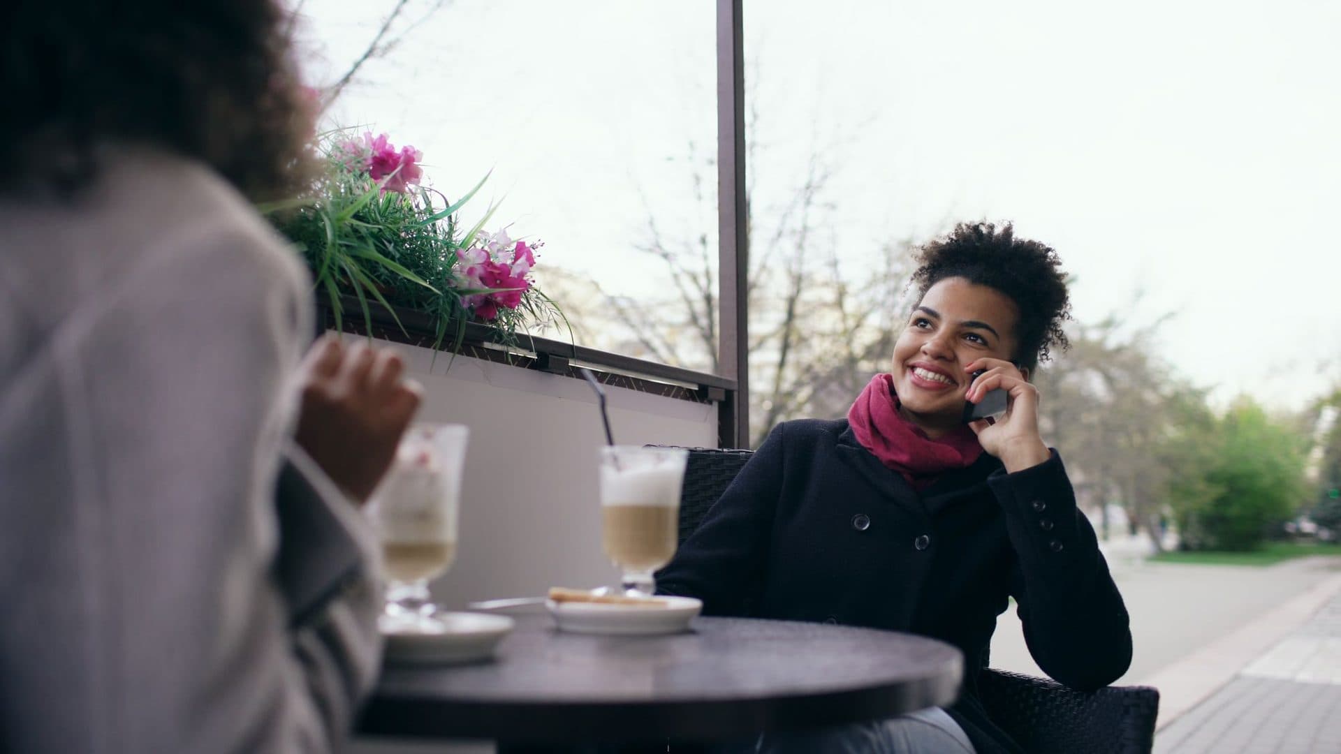A smiling woman taking a phone call at a cafe table