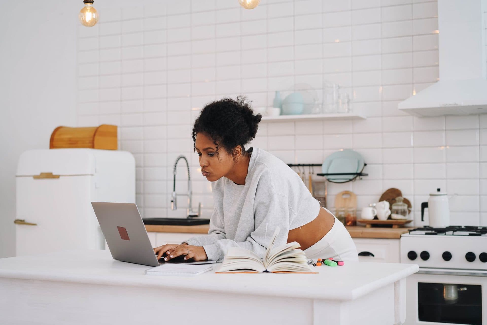 A woman at a bright kitchen counter typing on a laptop